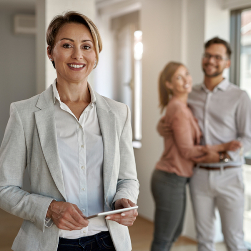 Portrait of female real estate agent looking at the camera while happy couple in standing in the background.